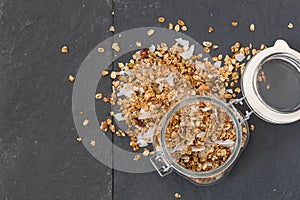 Glass jar of homemade organic granola with coconut and pecans on black background. Delicious breakfast cereal. muesli