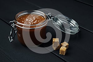 A glass jar with homemade salted caramel and a few pieces of brown sugar