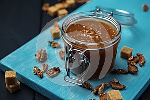 A glass jar of homemade salted caramel and fried walnuts with pieces of cane sugar