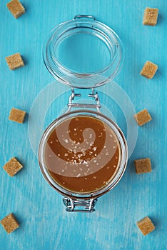 A glass jar of homemade salted caramel with pieces of cane sugar