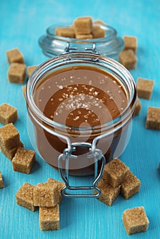 A glass jar of homemade salted caramel with pieces of cane sugar