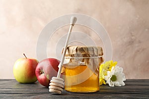 Glass jar with honey, dipper, apples and flowers on wooden background