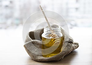 Glass jar with honey and a dipper inside stands on a sackcloth