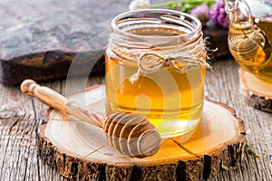 Glass jar of honey with honey dipper on wooden slice close-up