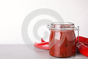 Glass jar of hot chili sauce with peppers on table