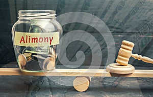 Glass jar and the inscription `Alimony` and the hammer of the judge are on the scales. Payment of alimony of one of the spouses. D photo