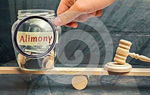 Glass jar and the inscription `Alimony` and the hammer of the judge are on the scales. Payment of alimony of one of the spouses. D