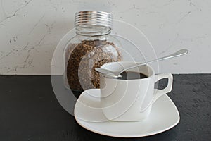 A glass jar of instant coffee in large granules next to a white mug