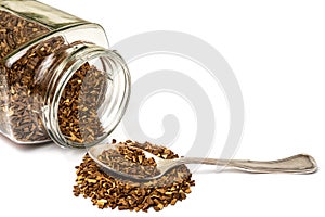 Glass jar of instant sublimated coffee and heap of scattered granules with silver spoon on white background