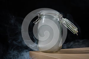 Glass jar with a lid filled with smoke on a black background. Fog in a transparent container on the table.