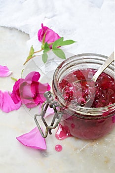 Glass jar and little spoon with tea rose petal jam on light marble background. Copy space for text.