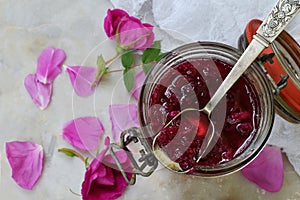 Glass jar and little spoon with tea rose petal jam on light marble background. Copy space for text.