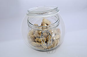 Glass jar with lots of peanuts on a white background