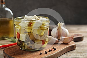 Glass jar of marinated feta cheese on wooden table photo