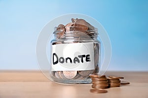 Glass jar with money and label DONATE on table