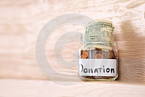 Glass jar with money and label DONATION on shelf against wooden background.