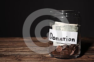 Glass jar with money and label DONATION on table against black background