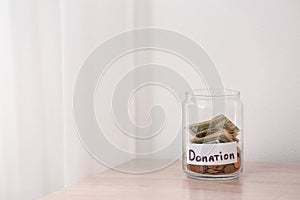 Glass jar with money and label DONATION on table against light background.