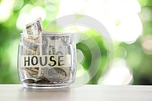 Glass jar with money and label HOUSE on table against blurred background