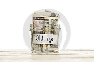 Glass jar with money for old age on wooden table against white background