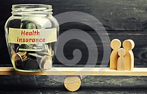 Glass jar with money and the words `Health Insurance` and the family on the scales. The concept of medical insurance of life, fami