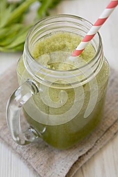 Glass jar mug filled with celery smoothie over white wooden background, side view. Close-up