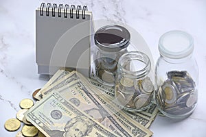 Glass jar with multicurrency coins, US dollar bills and white paper stand