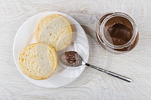 Glass jar with nut-chocolate paste, pieces of bread, teaspoon