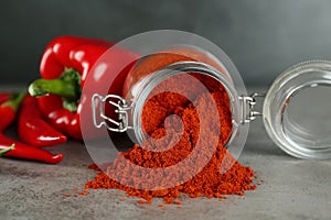 Glass jar of paprika with red peppers on light grey table, closeup