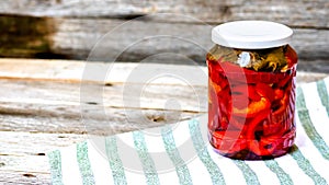 Glass jar with pickled red bell peppers.Preserved food concept, canned vegetables isolated in a rustic composition