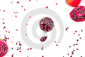 Glass jar with pomegranate seeds with spoon and sliced pomegranates, scattered seeds