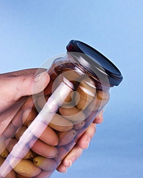 Glass jar of preserved olives in woman hand