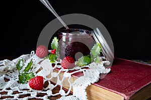 Glass jar of raspberry jam sitting on white doily.