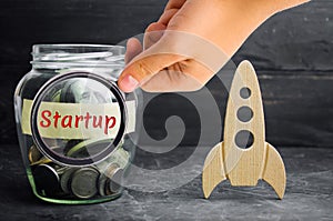 Glass jar, rocket and the word `Startup`. The concept of raising funds for a startup. Charitable contributions to translate ideas