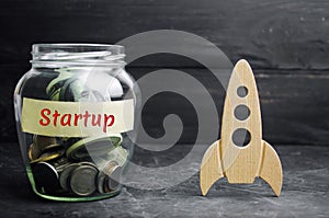 Glass jar, rocket and the word `Startup`. The concept of raising funds for a startup. Charitable contributions to translate ideas