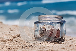 Glass jar with sea shells on the sandy beach, vacation time