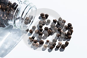 Glass jar with seasoning. Black pepper is scattered on white