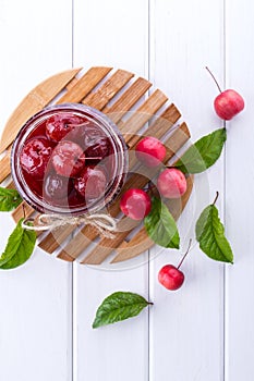 Glass jar of small paradise apple jam with fresh fruits on white table. top view