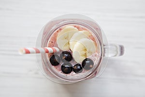 Glass jar with smoothie made of banana, black currant, coconut milk on a white wooden background, top view.