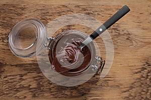 Glass jar and spoon of chocolate paste on wooden table, top view