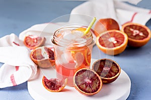 Glass Jar of Squeezing Juice from Orange Cold Orange Juice with Red Orange Ice Cubes Healthy Drink Blue Background