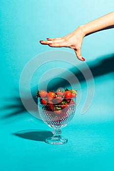 Glass jar of strawberries on a blue background and woman`s hand with painted nails above.