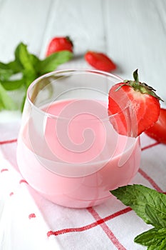 Glass jar of strawberry milkshake and ingredients on white wooden table