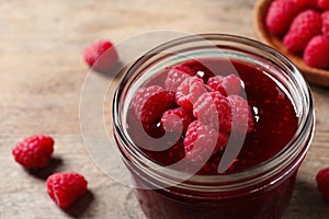 Glass jar of sweet jam with ripe raspberries on wooden table