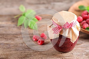 Glass jar of sweet jam with ripe raspberries on wooden table