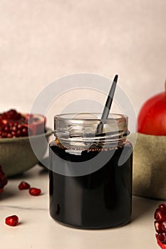 Glass jar of tasty pomegranate sauce on white marble table