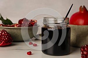 Glass jar of tasty pomegranate sauce on white marble table. Space for text