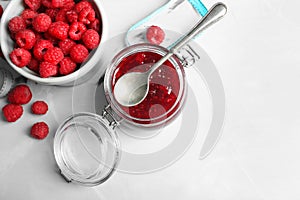 Glass jar with tasty raspberry jam on light table