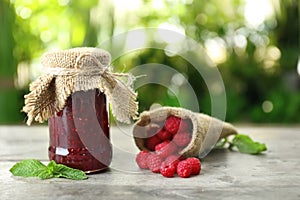 Glass jar with tasty raspberry jam on table against blurred background