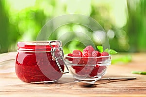 Glass jar with tasty raspberry jam on table against blurred background